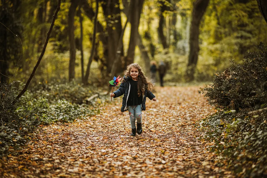 Kind rennt ueber einen Waldweg voller Laub - Familienfotos Herbst